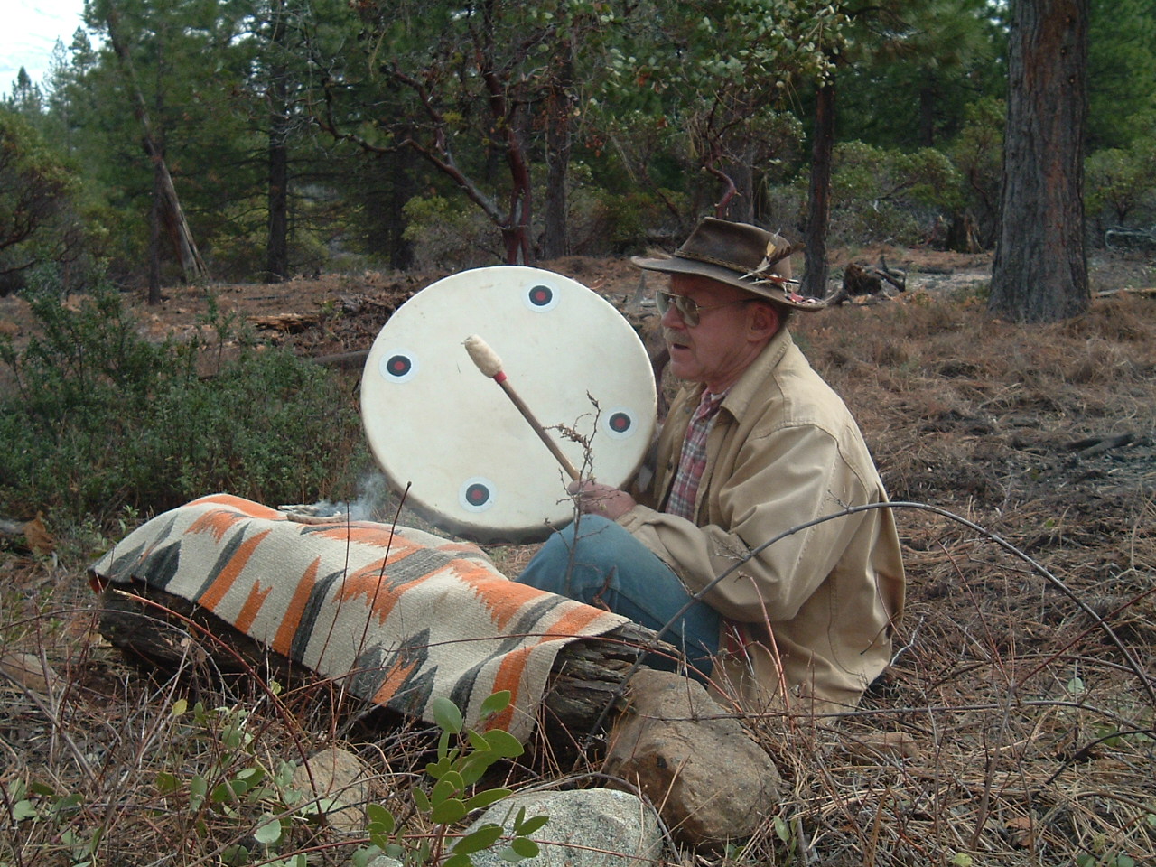 Image of John P Brennan sitting at the edge of a forest drumming.