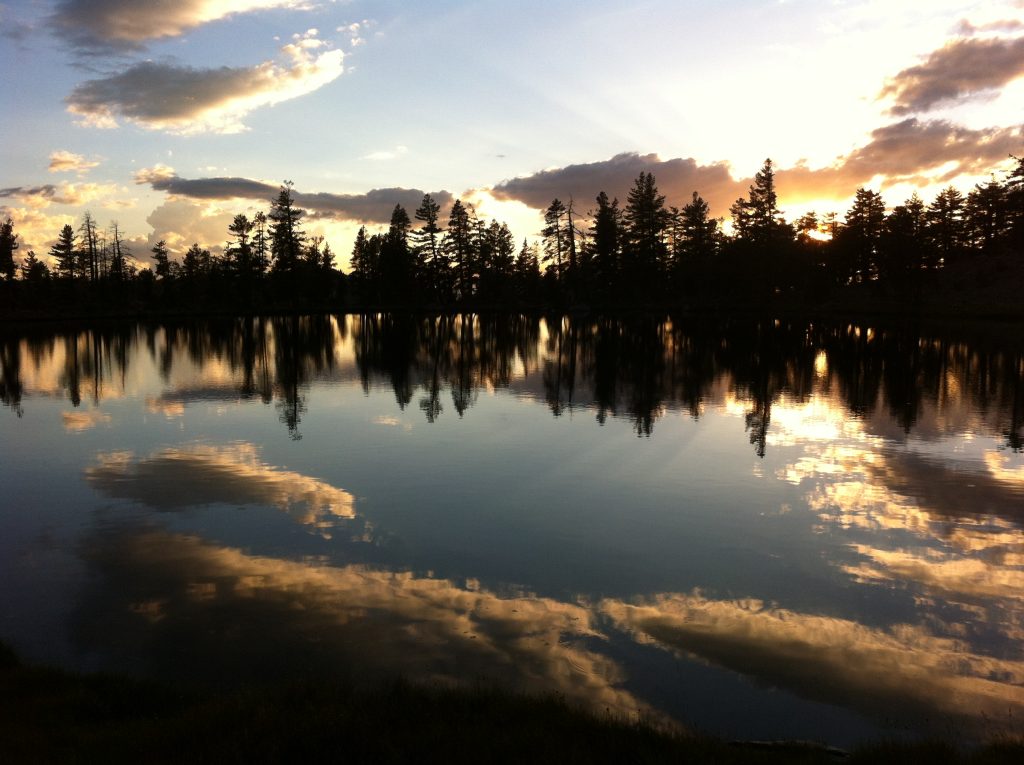 near ravensites, a photo of upper deadfall lake at sunrise with clouds and coniferous trees reflecting in the water reminds us to take time to reflect